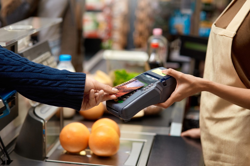 A shopper paying at a grocery checkout while citrus sits on the scale