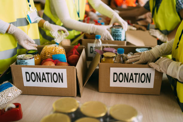 Hands filling boxes labeled donation with food and supplies